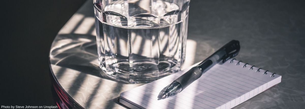 glass of water on a table with a notepad and pen