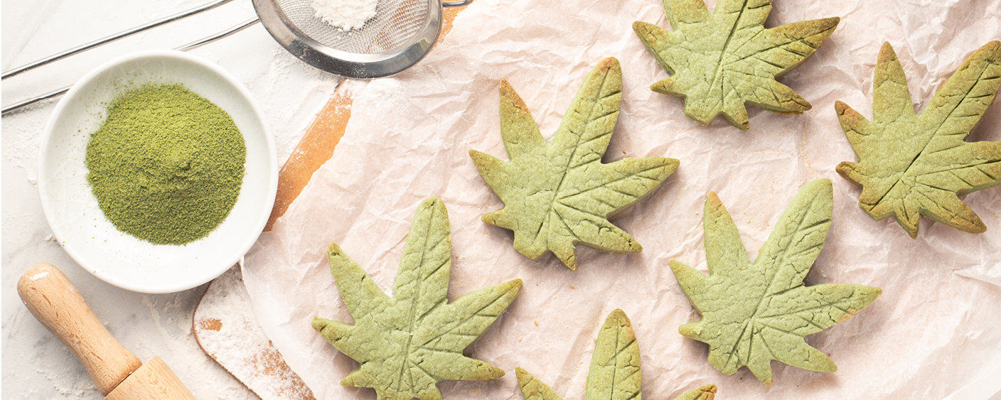 cannabis leaf shaped sugar cookies on parchment paper with flour and rolling pin