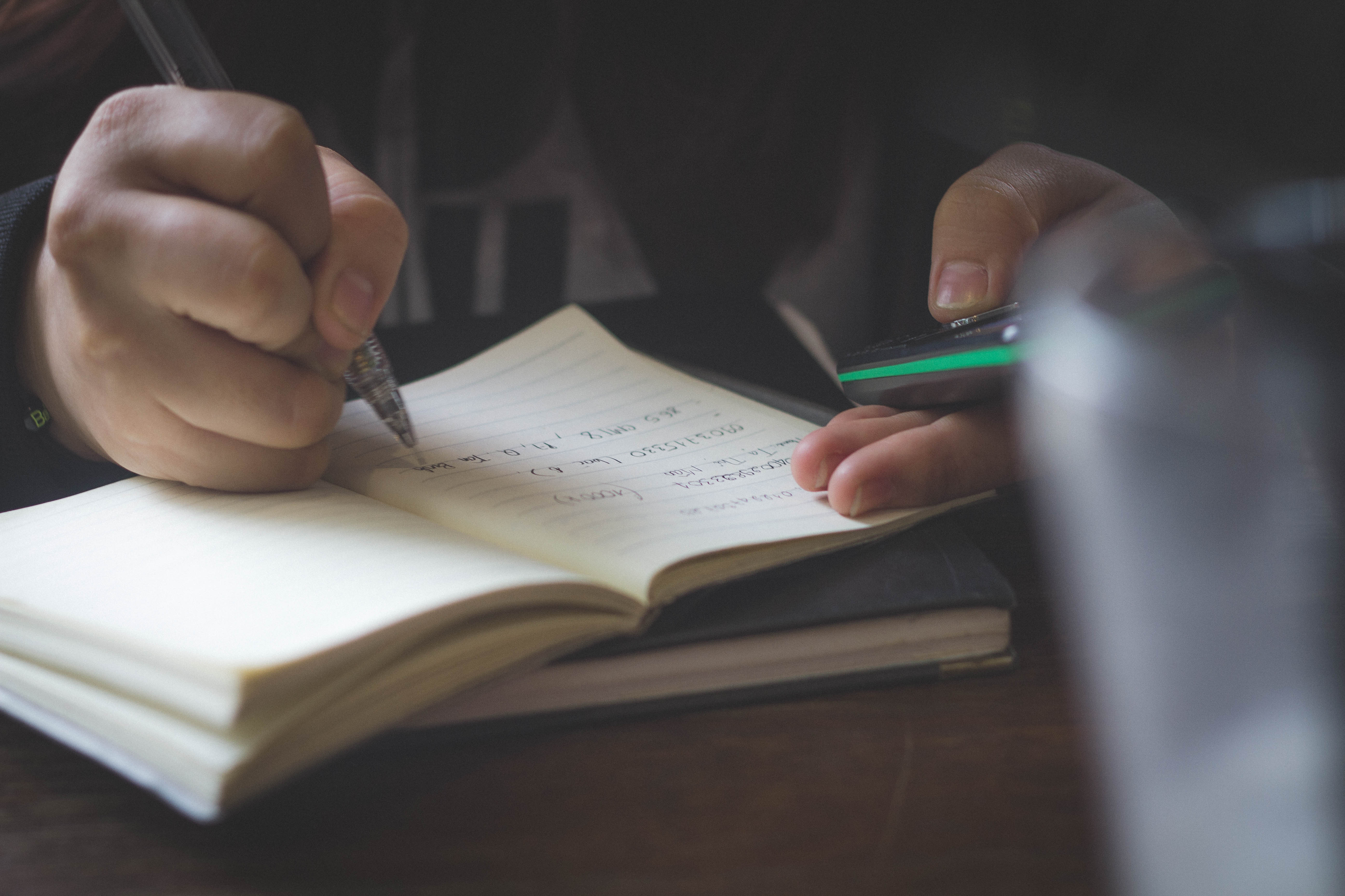 A person taking notes and looking at their phone, meant to demonstrate how to do research before you talk to your doctor about medical cannabis